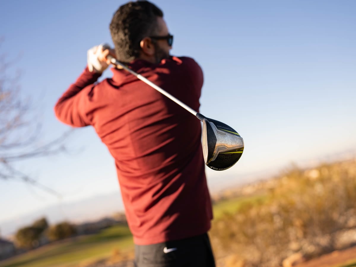 Golfer at full follow-through watching a drive down a desert course at sunset