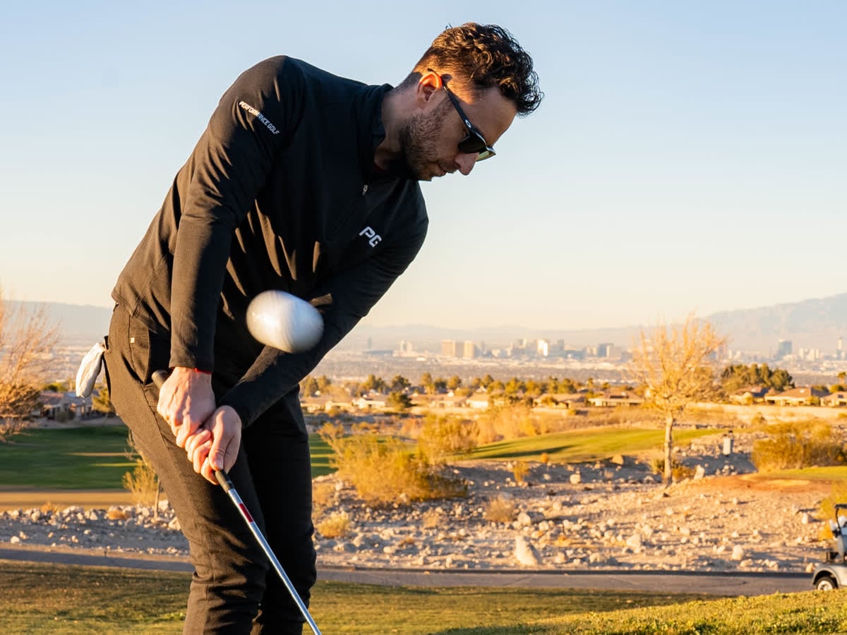 Golfer flighting a chip shot at golden hour with the ball frozen in mid-air
