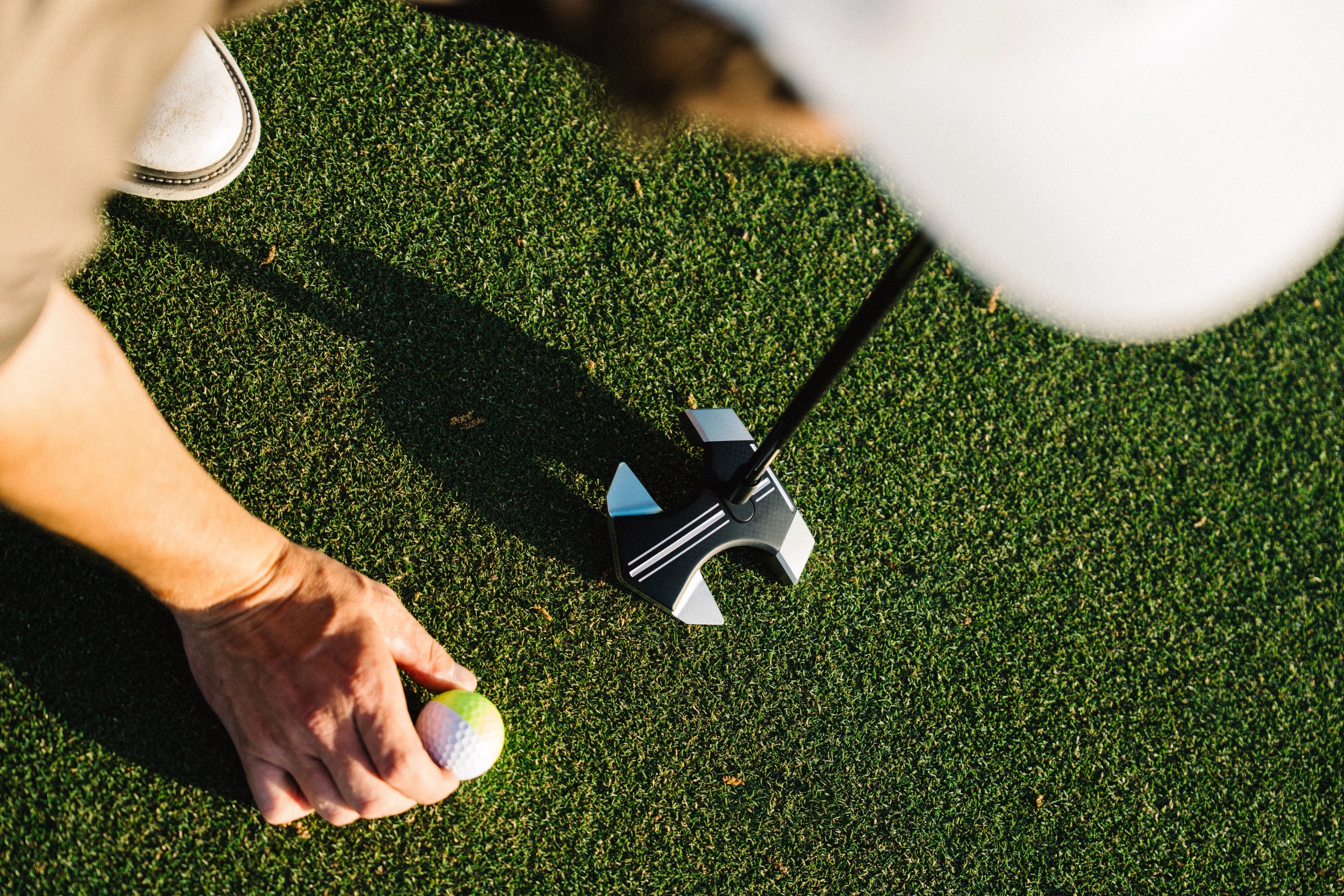 Overhead view of golfer picking up ball beside RS1 putter on the green