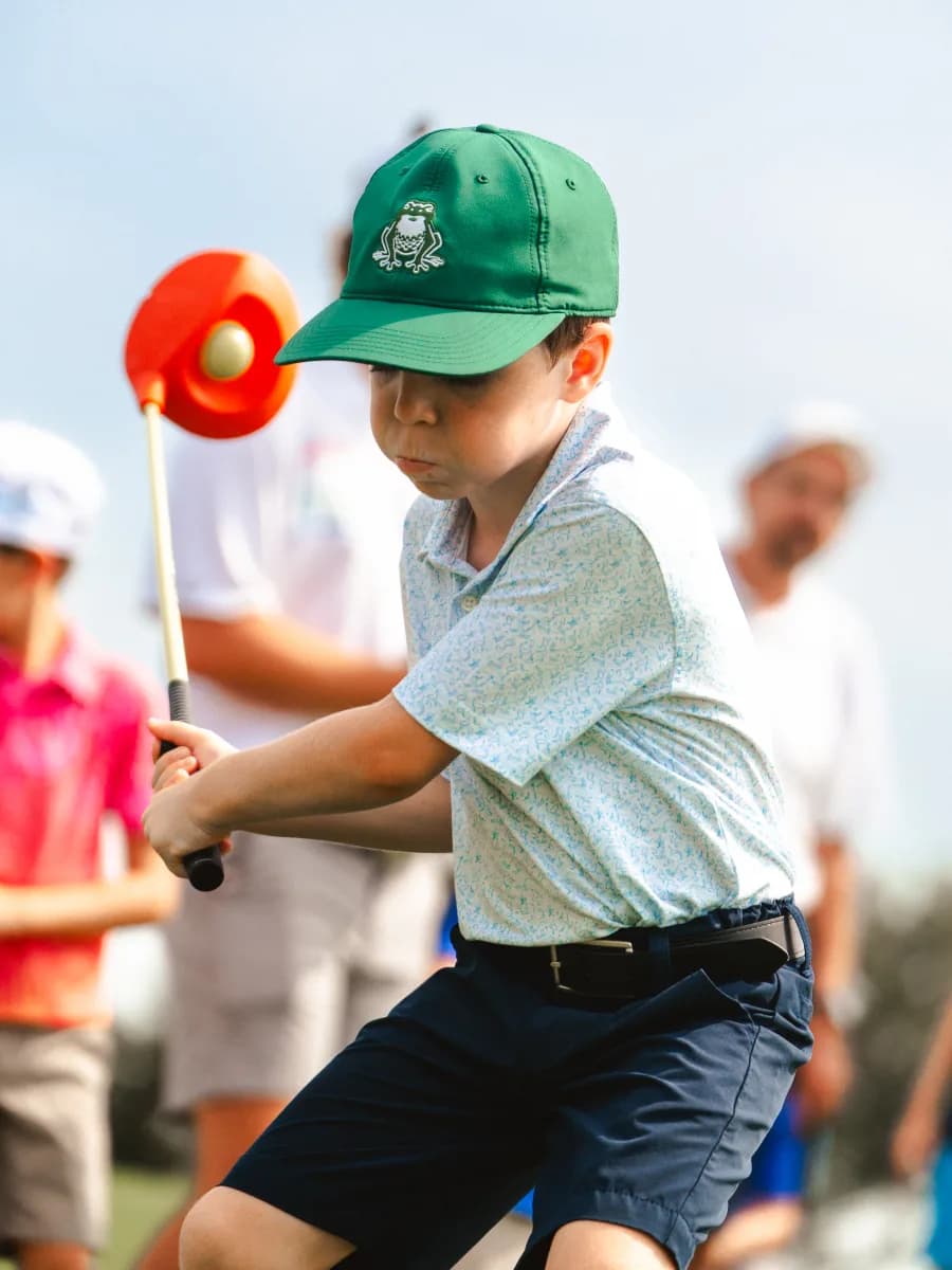 Toddler in setup with yellow club, smiling at the yellow ball on the tee
